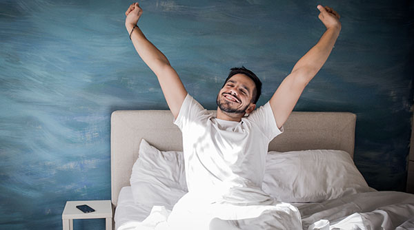 ALT Text: a man in a white t-shirt stretching his arms like is just waking up