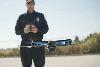 ALT Text: a man controlling a blue drone wearing all black with black sunglasses