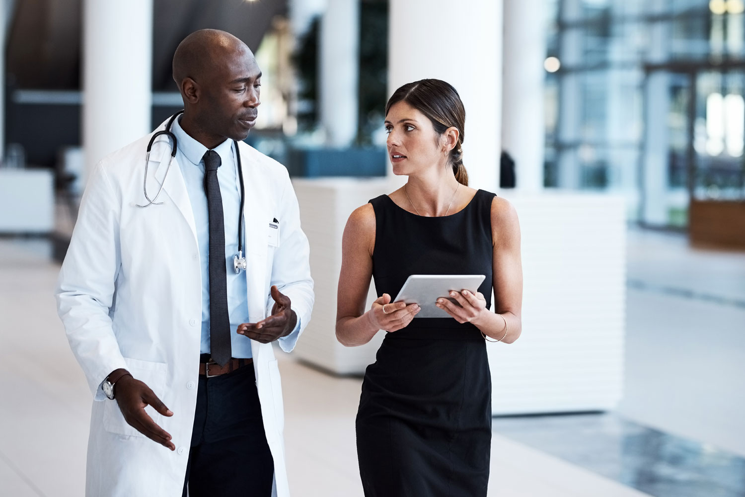 ALT Text: a male Doctor talking with a woman holding a tablet talking.