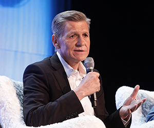 ALT Text: side view of Marc Pitchard speaking to the audience while holding up a mic